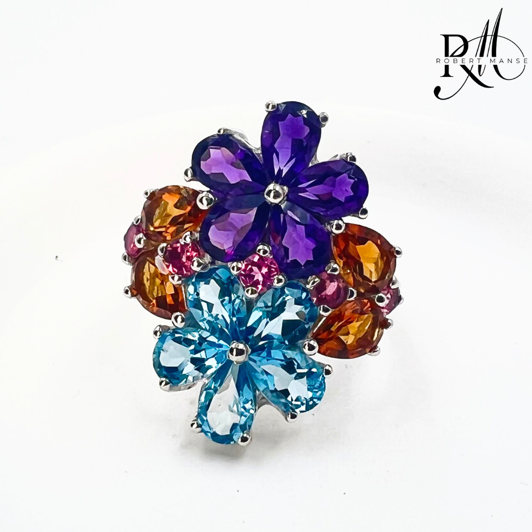 A rhodium silver multi-stone flower ring with pear-shaped blue topaz, round rhodolite, and citrine gemstones.