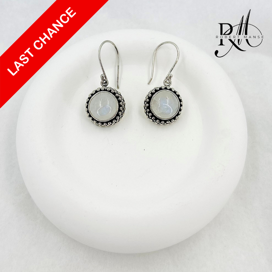 Pair of silver earrings with circular designs on a white surface, with a red banner and brand logo in the corner.